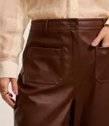 Pantalón recto de cintura alta confeccionado en poliuretano simil cuero marrón, con trabillas en la cintura, bolsillos delanteros y cierre tradicional.
