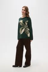 Sweater de punto jacquard con diseño floral abstracto en tonos tierra sobre fondo negro, de corte holgado, cuello redondo y manga larga.