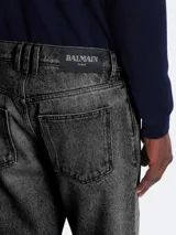 Jeans Balmain de corte regular fit, confeccionados en denim de algodón con lavado desgastado en tono gris oscuro. Presentan diseño de cinco bolsillos, cierre frontal con botones y costuras reforzadas.