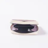 Monedero de cuero sintético texturizado color blanco, con cierre perimetral y tarjetero exterior con detalles en color lila.