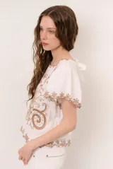 Blusa blanca de manga corta con detalles de bordados y perforaciones, cuello redondo y diseño holgado.