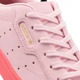 Championes Adidas modelo Sleek W, de diseño minimalista en color rosado con suela de goma translúcida en tono rojizo. Presenta perforaciones laterales características de la marca y logo dorado en el lateral.
