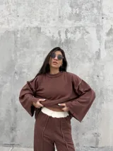Buzo oversize de color marrón chocolate, con cuello redondo, mangas anchas y diseño con costuras expuestas en contraste. Presenta terminaciones desflecadas en el ruedo y en los puños.