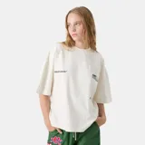 Remera oversized color blanco crema, con cuello redondo y mangas cortas. Presenta un estampado en la espalda con el logo de "Eme Studios" en verde y texto "Building a community through gratitude".