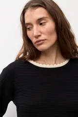 Sweater de punto negro con escote bote, mangas largas y detalles de terminación en ondas de color blanco en el cuello, los puños y el ruedo.