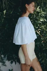 Short de tiro alto en denim de algodón levemente elástico, color beige, con bolsillos delanteros de parche con ribete y cierre frontal con botón.