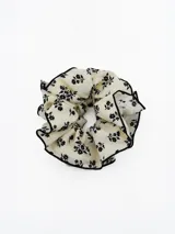 Colita para el pelo tipo scrunchie de tela color crema con estampado floral negro y borde con terminación en hilo negro.