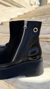 Botas cortas de cuero combinado en tonos tostado, marrón y detalles en charol negro. Cuentan con suela chunky, taco de 6 cm, cierre lateral y laterales de gamuza.