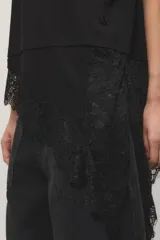 Remera negra de corte oversize, con escote redondo, mangas cortas y detalle de tajo irregular con terminación en puntilla en el ruedo. Confeccionada en jersey de algodón.