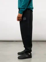 Pantalón de jogging de felpa con friza, color gris, con cintura elástica, bolsillos laterales y puños en los tobillos. Presenta un parche con el logo de Umbro en la parte superior delantera.