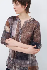 Camisa de corte recto con cuello mao y cierre frontal parcial de botones. Presenta un diseño estampado tipo patchwork con motivos florales y geométricos en tonos tierra, marrones y beige. Posee mangas tres cuartos con puños simples.