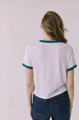 Remera de manga corta estilo ringer, color blanca con ribetes verde oscuro en cuello y puños. Cuenta con estampado frontal de Coca-Cola en color verde.
