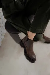 Bota tipo chelsea de punta redonda, confeccionada en una combinación de cuero texturizado y gamuza en tonos marrones. Presenta elásticos laterales negros y una suela track robusta de goma negra.
