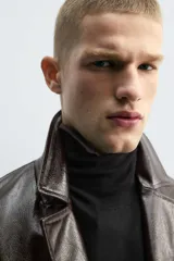 Cazadora cropped de hombre confeccionada en tejido efecto piel de acabado brillante y color marrón. Cuenta con cuello de solapas de muesca, manga larga con puños abotonados, bolsillos de vivo en la cadera y cierre frontal con botonadura.