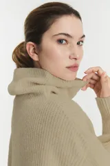 Sweater de punto acanalado en color beige, con cuello alto tipo tortuga, mangas largas con puños ajustados y diseño holgado.