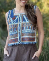 Chaleco corto en denim con bordado artesanal multicolor y escote cuadrado. Con cierre de botones y terminaciones desflecadas.