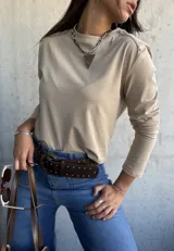 Remera de algodón color beige, de manga larga y cuello redondo, con detalle de tachas metálicas en los hombros.