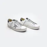 Zapatillas de cuero blancas con aplique de estrella gris, talón negro, cordones grises de algodón y suela de caucho.