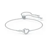 Pulsera Swarovski bañada en rodio, con cadena fina plateada ajustable. Presenta un dije con el símbolo del infinito entrelazado a un corazón, ambos adornados con pequeños cristales blancos.