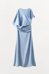 Vestido midi de tejido satinado color celeste, con cuello barco y diseño asimétrico con mangas tipo capa. Presenta un detalle drapeado en la cintura y abertura en la espalda.