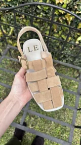 Sandalias de cuero marrón con diseño de tiras entretejidas y hebilla lateral.