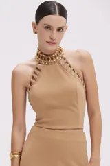 Top cropped de crepé color beige, con cuello halter alto decorado con pedrería y aberturas en los tirantes.