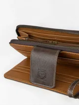 Billetera grande de cuero con estampado animal print tipo leopardo y detalles en cuero marrón. Cuenta con una correa de muñeca incorporada y cierre con solapa y broche grabado.