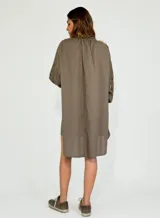 Vestido corto de corte holgado, con cuello camisero y cierre frontal de botones. Presenta mangas tres cuartos con detalles de encaje calado en los laterales y dobladillo asimétrico.