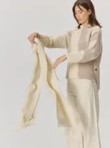 Bufanda de gran tamaño en color mostaza con diseño de tejido en espiga y flecos en los extremos. Incluye una etiqueta metálica decorativa en una de las esquinas.