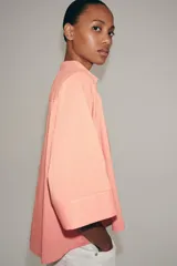 Camisa ZARA Woman Collection confeccionada en hilatura con viscosa, con diseño de rayas finas y color salmón. Presenta cuello perkins, mangas por debajo del codo, bajo asimétrico y cierre frontal cruzado con botones.