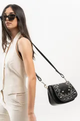 Bandolera de cuero negro con estructura rígida, tapa frontal decorada con tachas metálicas plateadas colocadas a mano y correa larga ajustable.