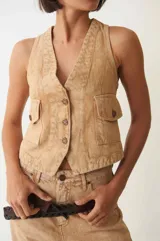 Chaleco denim color arena con efecto acid wash, cuello en V, cierre frontal con botones y dos bolsillos con solapa en el pecho.