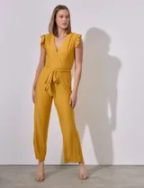 Mono de seda fría color mostaza, con escote en V cruzado, cintura elastizada con lazo de ajuste, espalda con abertura ojal y botón, y forro en el torso a tono.