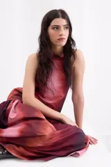 Vestido largo de corte holgado con estampado degradé en tonos rojizos y bordó. Presenta escote halter con cuello alto, espalda descubierta con cierre de botones y un maxi volado en la cadera que aporta volumen a la falda.