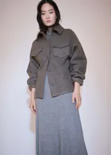 Chaqueta de tejido bouclé color gris oscuro, con diseño recto, cuello camisero, cierre frontal de botones y dos bolsillos de solapa con botón en el frente.