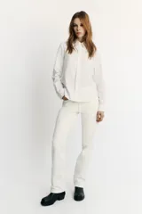 Camisa blanca de manga larga con cuello redondo tipo bebé y cierre frontal de botonadura simple.