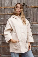 Parka liviana color beige con capucha, cierre frontal con botones, bolsillos delanteros con tapa y ajuste en la cintura. Presenta mangas con puños vueltos y detalle de botones.