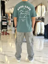 Remera oversize verde con estampado gráfico en la espalda con diseño de paisaje oriental y texto.
