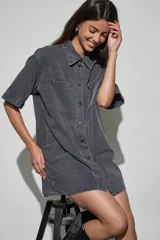Vestido corto de denim azul oscuro, con cuello camisero, mangas cortas, cierre frontal de botones y dos bolsillos en el pecho.