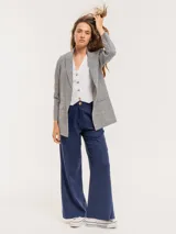 Pantalón de lino color beige, de tiro alto, pierna ancha y levemente acampanada. Tiene pinzas delanteras, elástico en la pretina trasera, cierre delantero y broche interno, bolsillos laterales y dobladillo invisible.