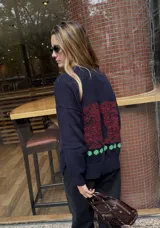 Buzo de punto color azul marino con diseño de conejos bordados a mano en la espalda en tonos rojizos y detalles de puntos verdes en el ruedo. Presenta cuello redondo y mangas largas.