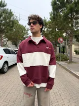 Buzo tipo polo de corte relajado y fit boxy, con diseño de bloques de color en bordó y blanco. Presenta cuello camisero con cierre frontal parcial y logo bordado en el pecho.