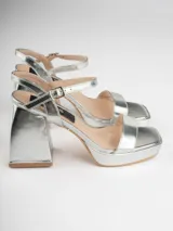 Sandalias plateadas con plataforma y tacón cuadrado, tira ancha sobre los dedos y pulsera con hebilla al tobillo.