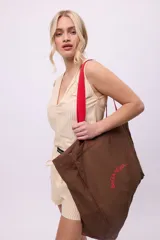 Bolso tote bag color marrón con asas rojas, logo "B&GANESHA" estampado en rojo y bolsillo interno con cierre. Incluye un porta termo.