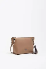 Bolso bandolera de estructura rígida y tamaño mediano confeccionado en piel vacuna. Presenta asa regulable, cierre con cremallera, bolsillo interior y logo metálico de la marca. Incluye un charm decorativo con borlas en el lateral y acabados metálicos.