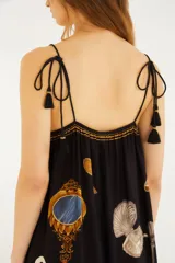 Vestido largo negro de silueta fluida, con finos breteles y detalle fruncido en la parte superior. Presenta un estampado exclusivo con elementos artísticos, palmeras, cisnes y otros motivos.