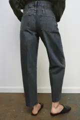 Jeans de tiro alto con corte barrel y diseño tapered, confeccionados en denim con efecto lavado y detalle de raya planchada. Presentan cintura con trabillas, cierre frontal con cremallera y botón, y bolsillos funcionales en delantero y espalda.
