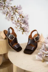 Sandalias de cuero negro con textura de reptil, diseño de punta cuadrada y taco bloque de madera. Presentan tiras cruzadas en el empeine y una hebilla metálica grande decorativa.