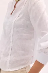 Blusa blanca de lino con escote en V y mangas largas con puños elásticos, combinando delantera estructurada de lino y espalda de algodón con spandex.