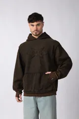 Buzo canguro de corte oversize, confeccionado en frisa de algodón con efecto de lavado gastado. Presenta un aplique decorativo cosido al corte en el centro del pecho, capucha amplia y bolsillo frontal tipo canguro.